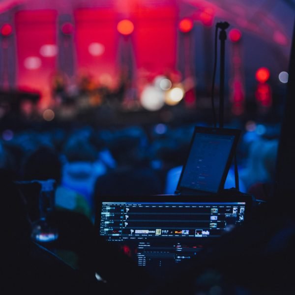 A horizontal shot of a party with lights, a stage and a turned-on computer for the DJ in a club